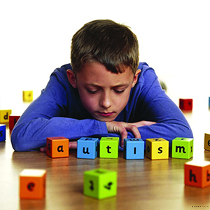 A boy resting his chin on his arms behind colourful letter blocks that spell the word autism.