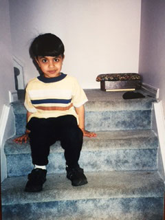 A young Qasim looking at the camera while sitting on carpeted stairs.