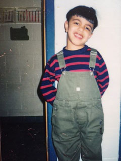 Qasim standing in striped overalls, smiling at the camera.