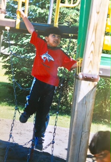 Qasim in a red shirt swinging from a backyard play structure.