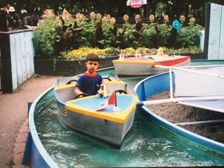 Qasim sitting in a small boat at an outdoor water-play area.