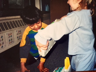 Qasim smiling as another child hands him a box during play.
